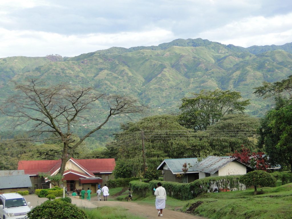 Kagando hospital nestled in a valley with a tree covered mountain in the background